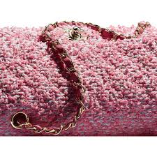 A detailed close-up of a pink tweed fabric classic flap bag, highlighting the rich textured material and the leather-interwoven chain strap, a perfect example of iconic Chanel designs.