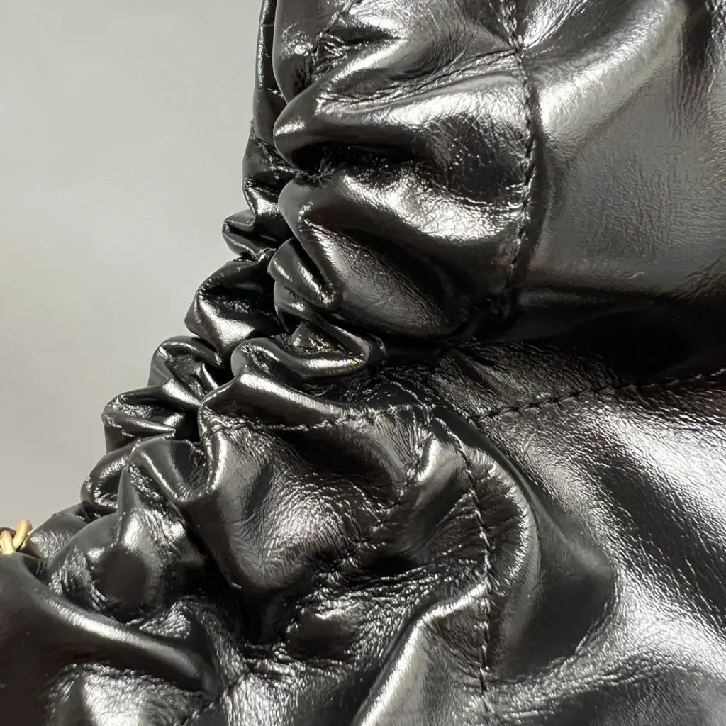Macro of glossy black quilted leather on a Chanel 22 Mini-style bag