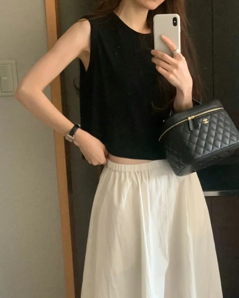 Chanel vanity case replica held beside a black sleeveless top and white skirt