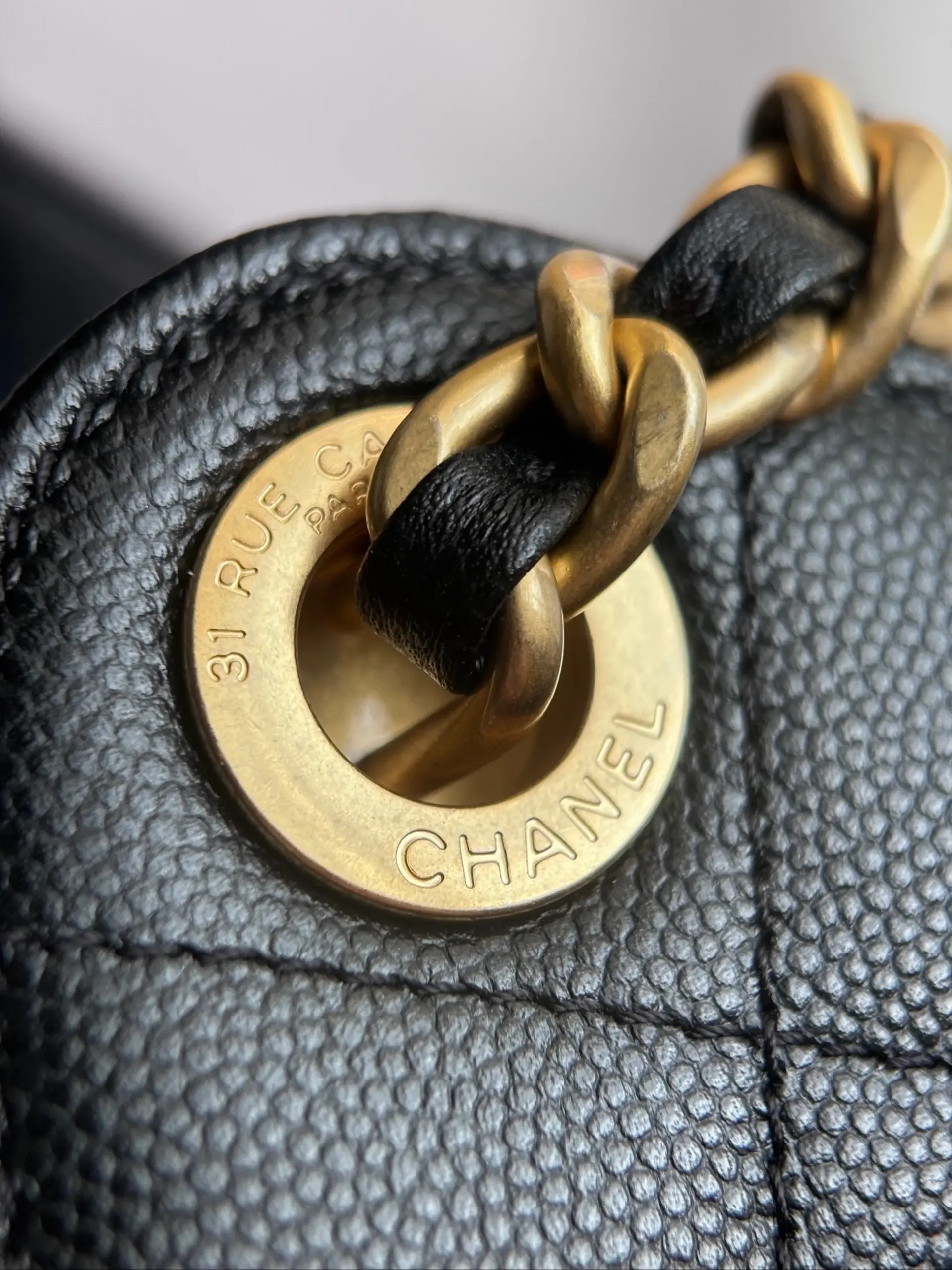 Macro of an engraved antique gold-tone eyelet and chain on black caviar leather