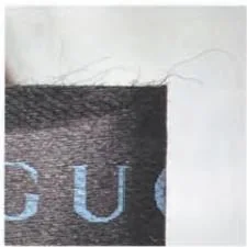 Top edge of a Gucci black fabric label with loose filaments visible above the print