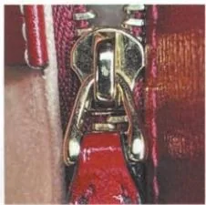 Gucci zipper slider and pull photographed beside red zipper tape